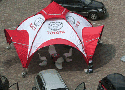 Kuppel Pavillon rund mit 5 Seiten und Eingangs-Dächern. Weiße Dachplane mit Toyota Logos, rote Entlüftungs-Spitze und rote Tunnel für die Aufnahme der Aluminium Stützen